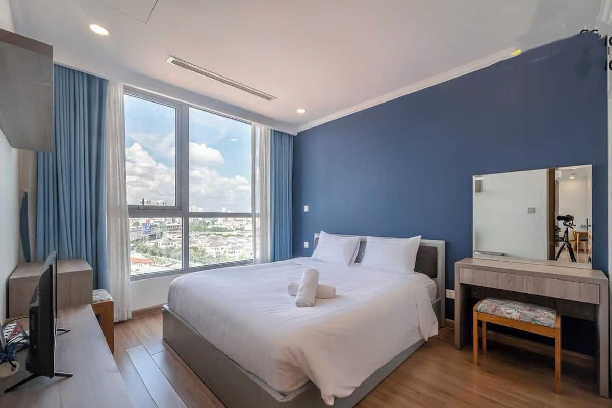 A modern hotel room with a large bed, a desk with a computer, a mirror, and a view of the city.