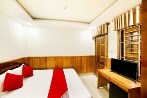 Quarto de hotel com cama, escrivaninha, televisão e guarda-roupa.