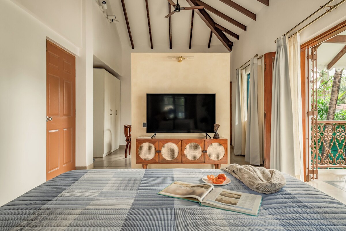 A bedroom with a large bed, a television on a wooden cabinet, and a view of the outdoors.