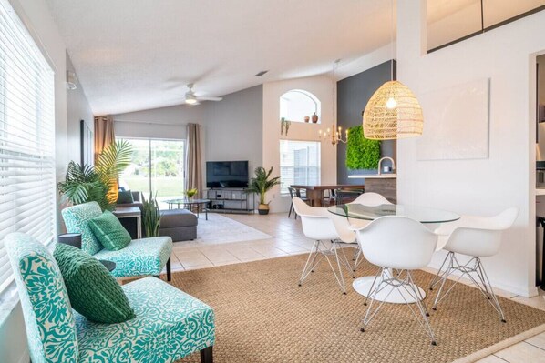 Un salon moderne avec un canapé, des fauteuils et un téléviseur. Il y a également un coin repas avec une table et des chaises.