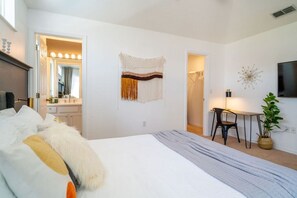 Une chambre moderne avec un grand lit, une coiffeuse avec un miroir, un bureau avec une chaise et un téléviseur fixé au mur.