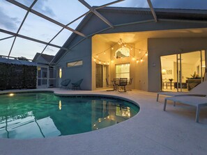 Une maison moderne dotée d’une piscine, d’un espace salon extérieur et de guirlandes lumineuses.