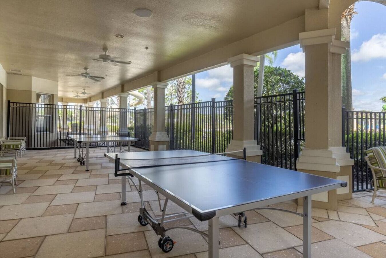 A covered outdoor area with ping pong tables, chairs, and a patio with a view of greenery.