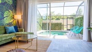 Una sala de estar moderna con un sofá verde, una mesa de centro de vidrio y vistas a una piscina y vegetación al exterior.
