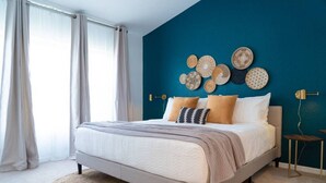 Un dormitorio con cama, cortinas, pared azul y una obra de arte en la pared.