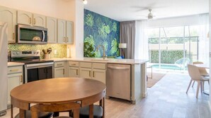 Una cocina moderna con una isla central, un comedor con mesa redonda y vista a una piscina.