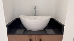 Un bagno con un lavabo a incasso bianco, un piano di lavoro nero e mobiletti marroni.