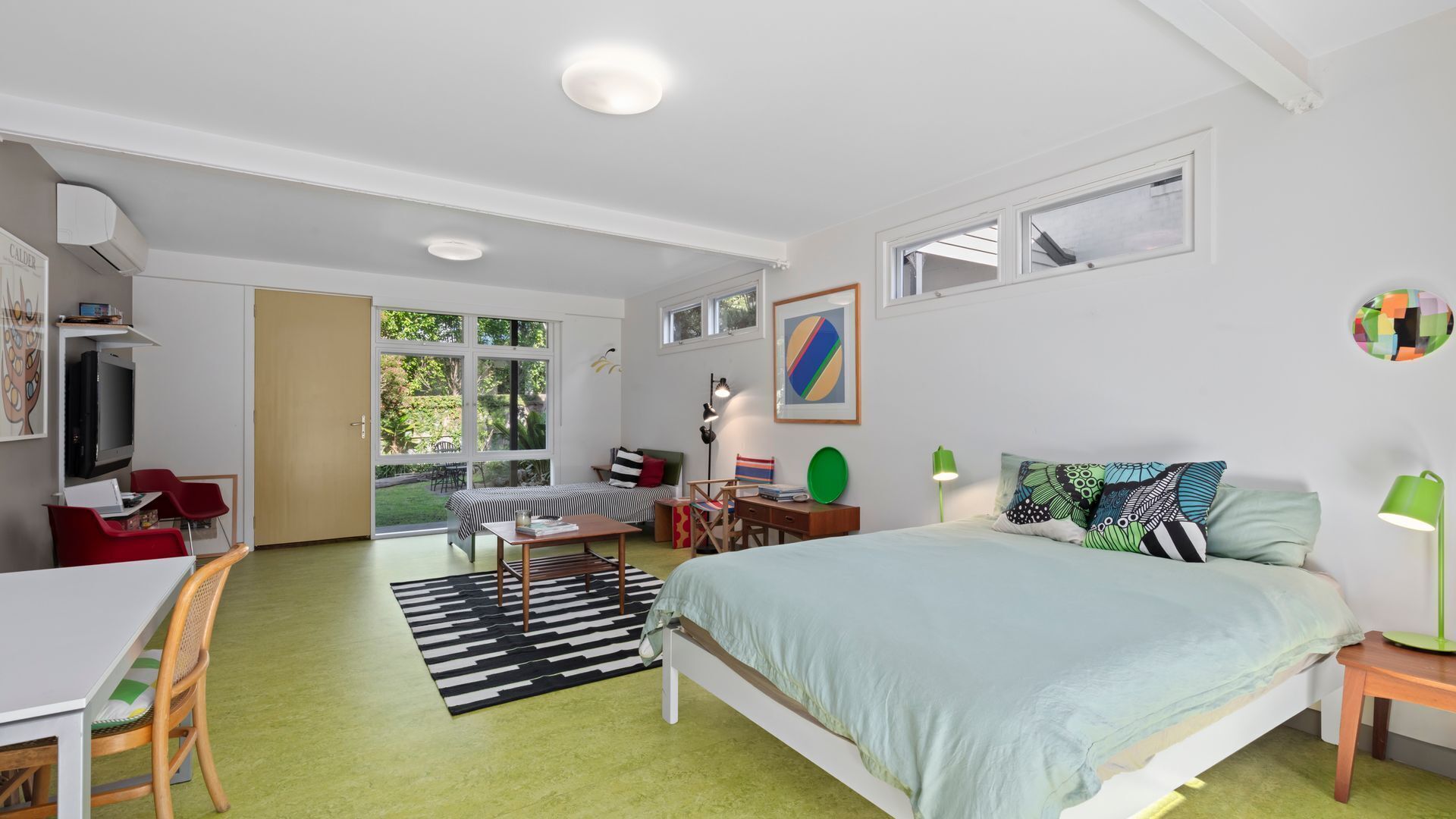 Une chambre moderne avec un lit, des tables de chevet, un bureau et une chaise. Une fenêtre laisse entrer la lumière naturelle et offre une vue sur l’extérieur.