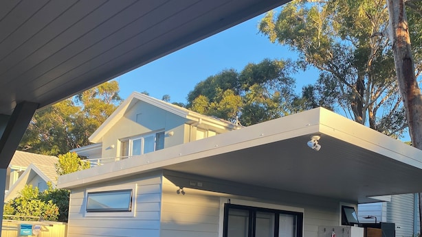Una casa moderna con una zona esterna coperta, caratterizzata da un patio in legno, un tavolo bianco e due sedie bianche.