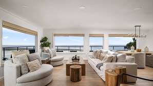 A spacious living room with a view of the ocean, featuring a large sofa, a coffee table, and a dining area.