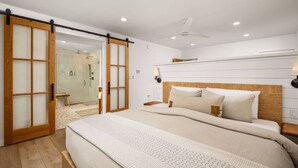 A bedroom with a bed, a headboard, a ceiling fan, and a sliding glass door leading to a shower area.
