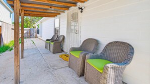A covered patio with wicker chairs and a smiley face mat. - Retreat with this charming home in Asian Town Houston. (Houston)