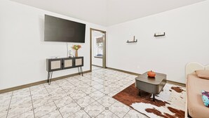 A modern living room with a flat-screen TV, a black console table, a small coffee table, a cowhide rug, and a white sofa with a cushion. - Retreat with this charming home in Asian Town Houston. (Houston)