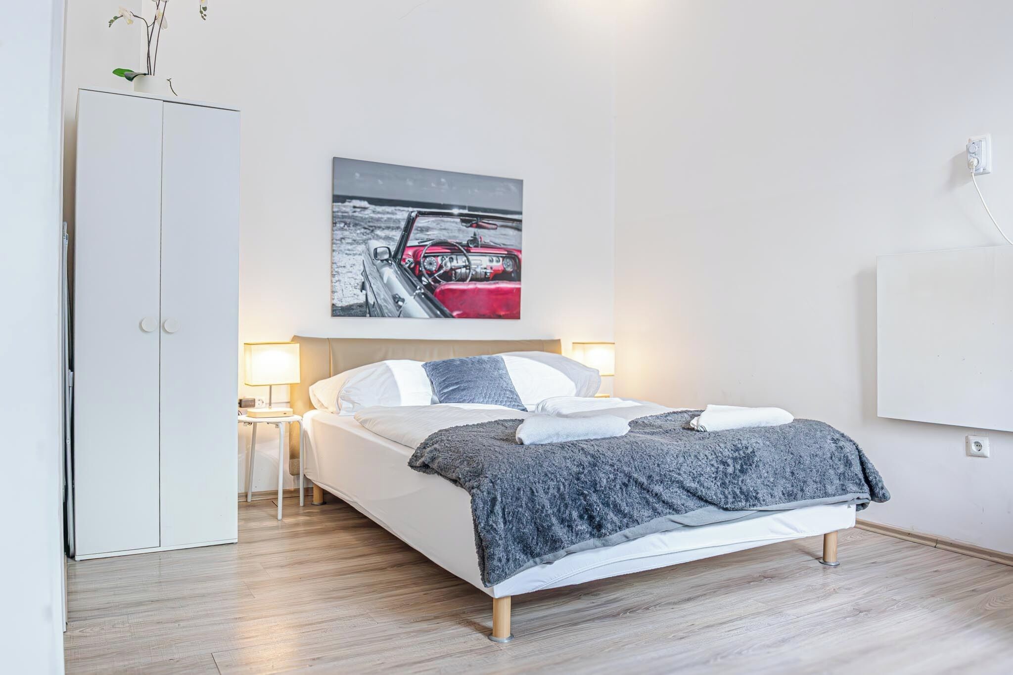 A modern bedroom with a bed, bedside tables, a wardrobe, and a wall-mounted artwork of a red car.