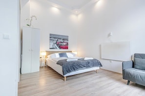 A modern bedroom with a bed, bedside tables, a grey sofa, and a painting of a red car on the wall. - Affordable Stay Near Wiener Stadthalle (Vienna)