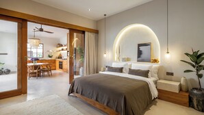 A modern bedroom with a large bed, bedside tables, and a curved wall light. - Modern Villa 2BR Casa Azuca by OriVista (Canggu)