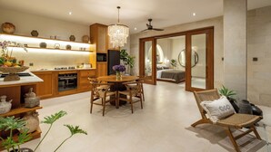 A modern kitchen with wooden cabinets, a chandelier, and a dining area with a round table and chairs. - Modern Villa 2BR Casa Azuca by OriVista (Canggu)