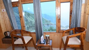 Una habitación de cabaña de madera con dos sillas de madera, una pequeña mesa y vistas a un paisaje montañoso a través de amplios ventanales.
