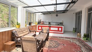 Una habitación amplia con un ventanal grande, un banco de madera, un tapete estampado y una zona de cocina con una decoración en blanco y rojo.