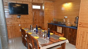 Comedor de madera con una mesa dispuesta para cuatro, un televisor montado en la pared y una zona de cocina con estufa y fregadero.