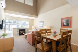 A spacious living room with a fireplace, a dining area with wooden chairs, and a large window providing natural light. - Glacier Lodge 340 NEW central AC just installed 2026 (Whistler)