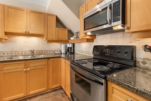 A kitchen with wooden cabinets, a stainless steel stove, a microwave, and a tiled backsplash.