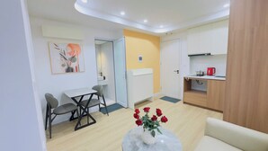 Un espacio habitable compacto con comedor, kitchenette y un pequeño rincón de estar con un jarrón de rosas rojas.