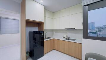 A modern kitchen with white cabinets, a black refrigerator, a stainless steel sink, and a window with a city view.