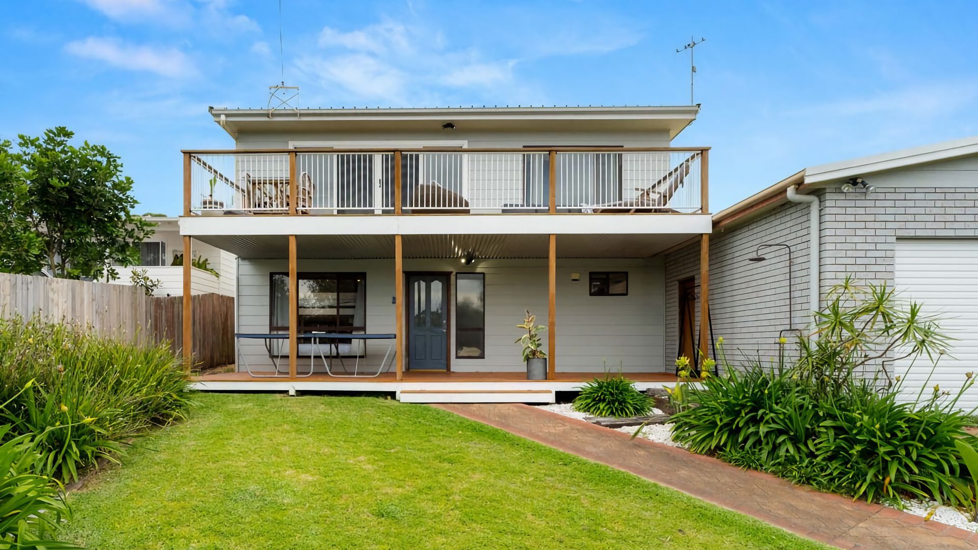Une maison à deux étages dotée d’un balcon, d’un porche couvert et d’un petit jardin.