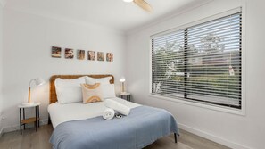 A bedroom with a bed, bedside tables, a ceiling fan, a window with blinds, and artwork on the wall. - Souira Beach House is pet friendly (Manyana)