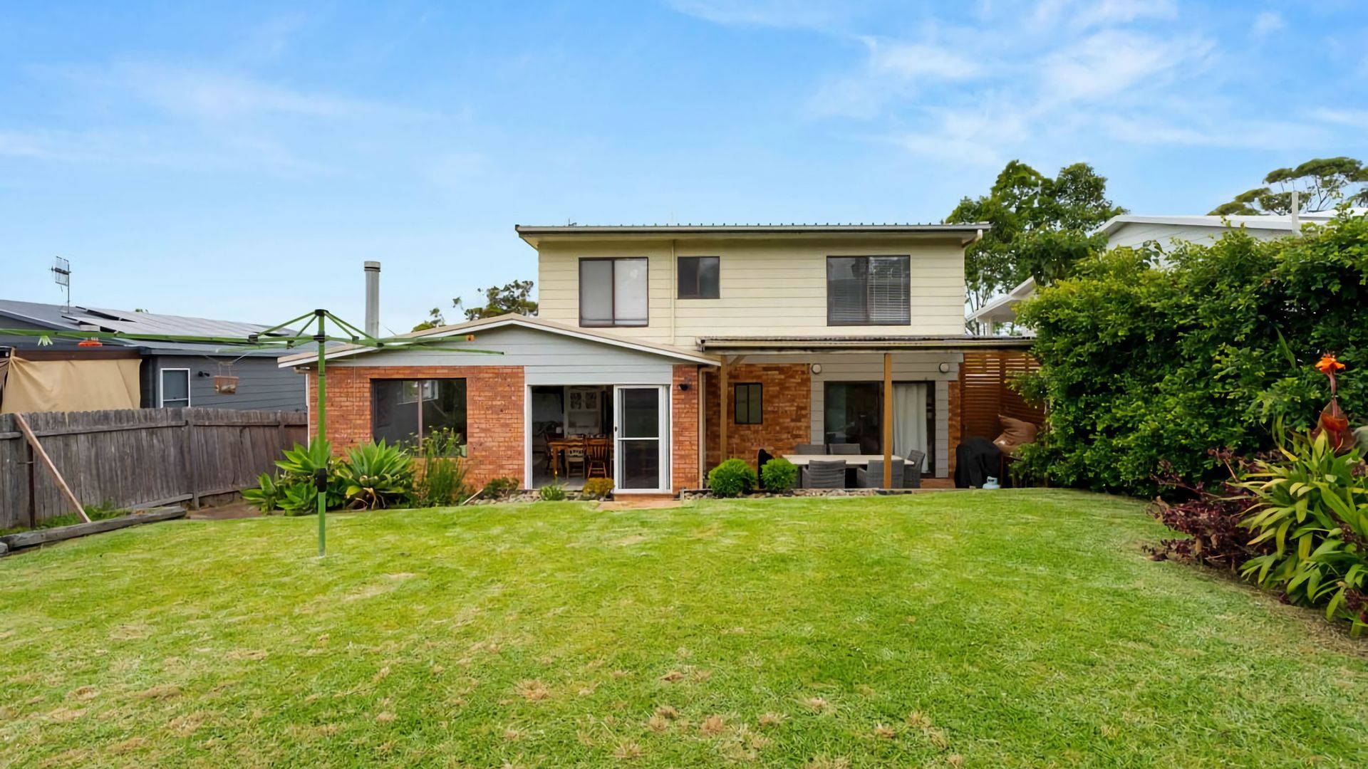 A two-story house with a covered patio, a fenced backyard, and a well-maintained lawn.