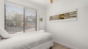 Ein Schlafzimmer mit einem Bett, einem Fenster mit Jalousien und einem an der Wand hängenden Kunstwerk.