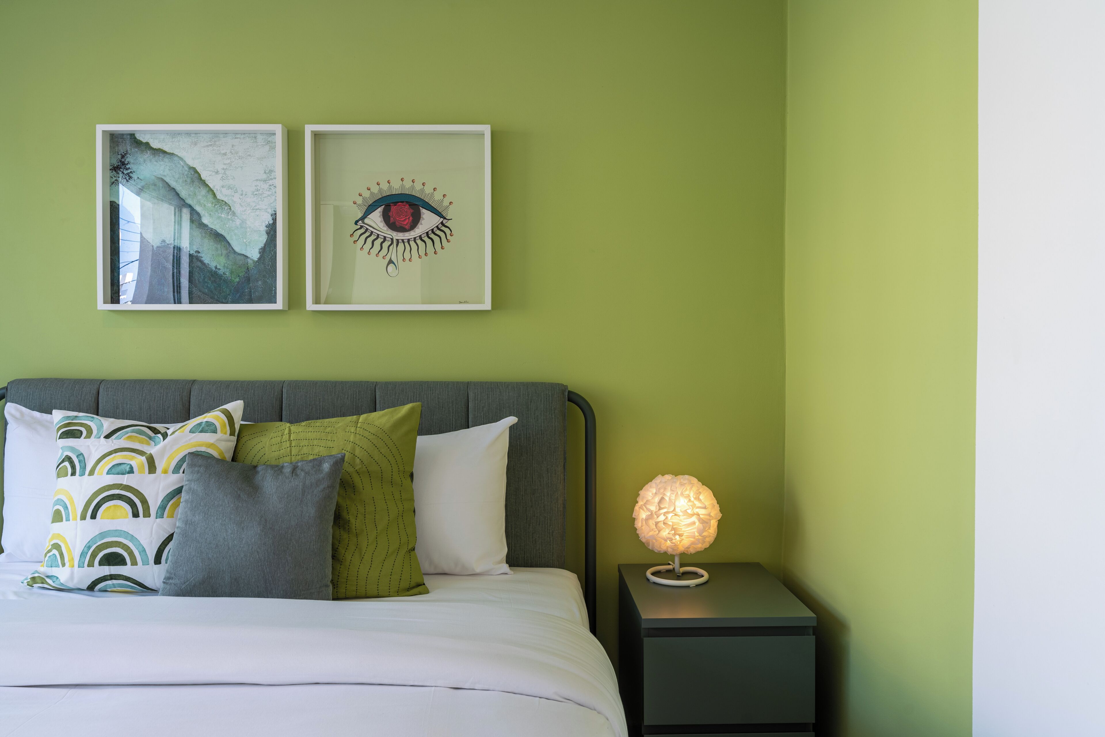 A bedroom with a bed, pillows, a nightstand, and two framed artworks on the wall.
