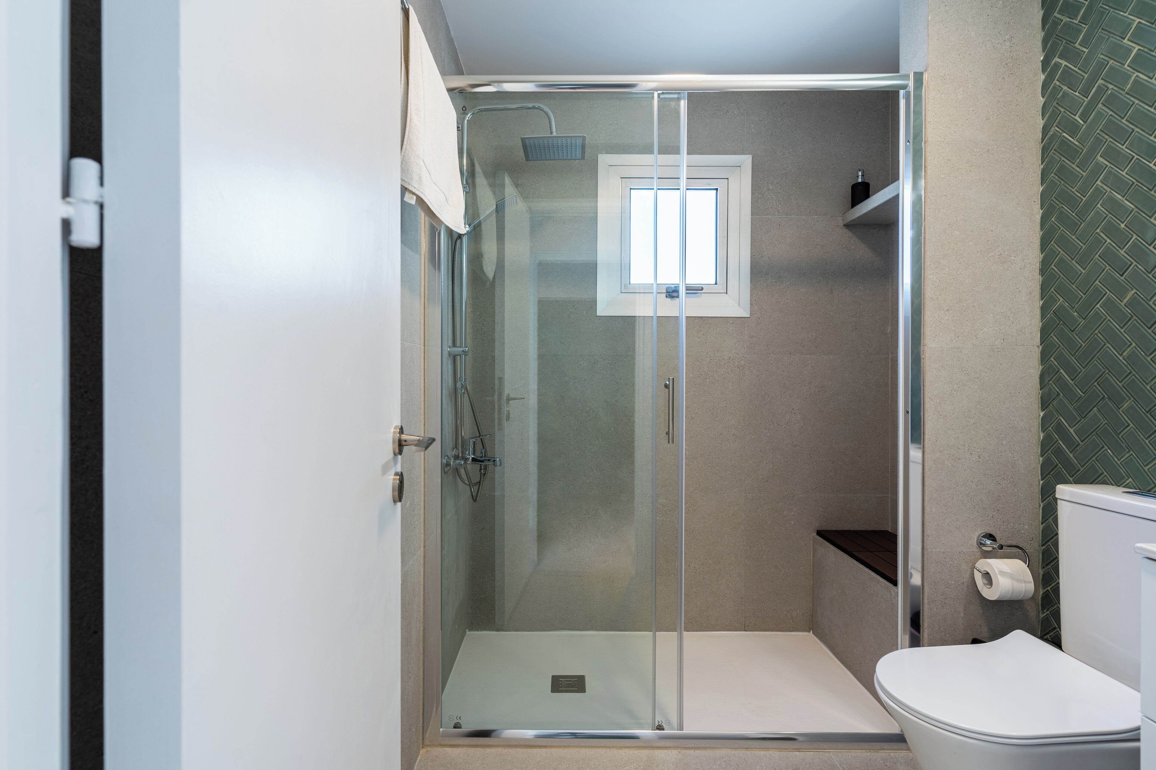 A modern bathroom with a glass-enclosed shower, a toilet, and a small window.