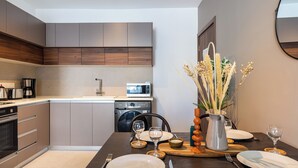 A modern kitchen with built-in appliances, a dining table set with plates, glasses, and cutlery. - Hazel 2-BR Apt. & Balcony in Larnaca (Larnaca)