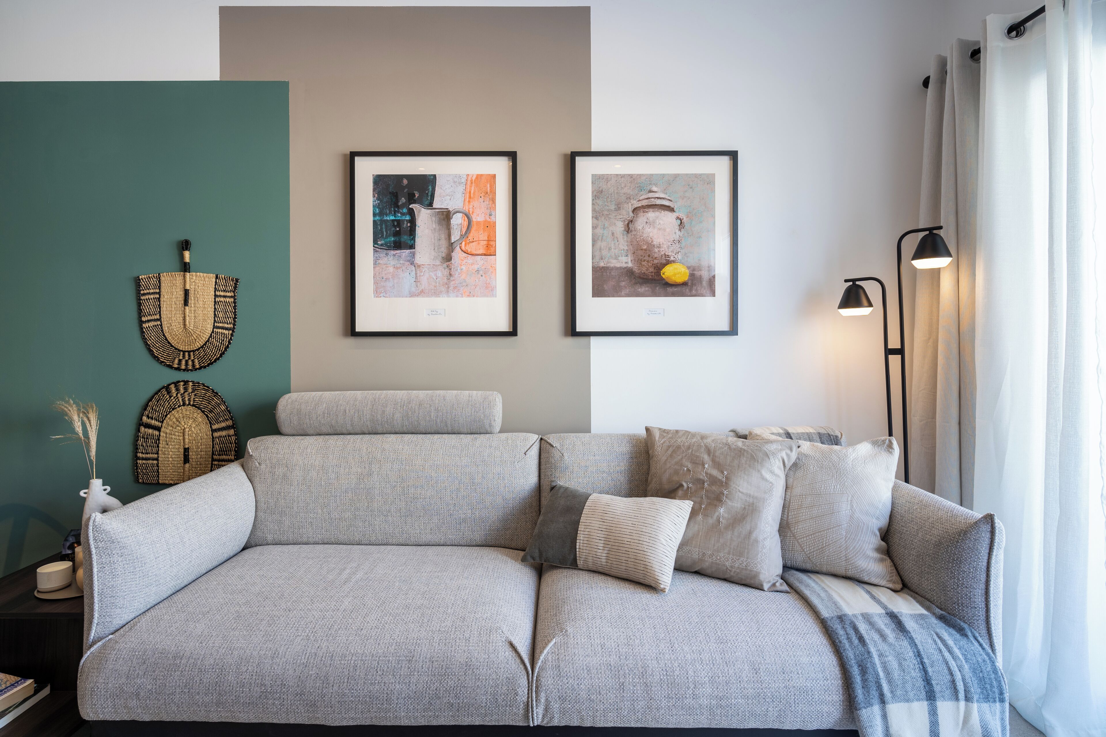 Uma sala de estar moderna com um sofá cinza, duas obras de arte emolduradas, um abajur e um enfeite de parede.