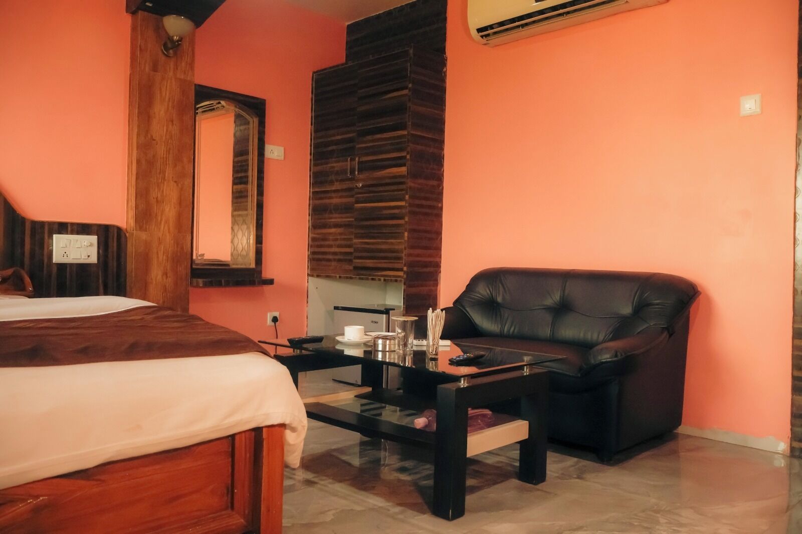 A hotel room with a bed, a leather armchair, a small table with a coffee maker, and a mirror.