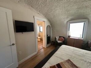 A bedroom with a bed, a television, a window, a mirror, and a door leading to a bathroom. - New! One-of-a-kind experience in the heart of Bear Lake! Hot Tub! Sleeps 8 + RV! (Garden City)