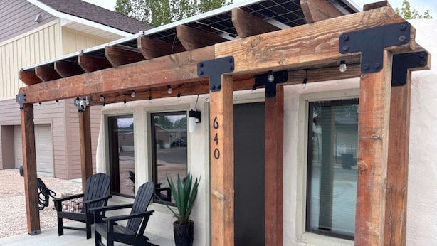 Une terrasse couverte avec deux fauteuils Adirondack et une plante en pot.