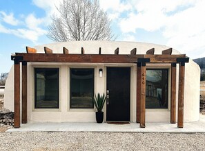 Un bâtiment moderne doté d’une pergola en bois, de grandes fenêtres et d’une plante en pot.