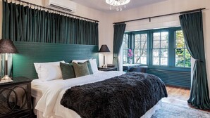 Une chambre à coucher avec un grand lit, une table de chevet, une lampe et une fenêtre avec des rideaux.