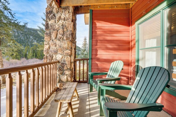 A wooden deck with a stone wall, a red building, and two green Adirondack chairs. - Walk to Ski Lift & Hot Tubs! Mtn-View Keystone Gem (Keystone)