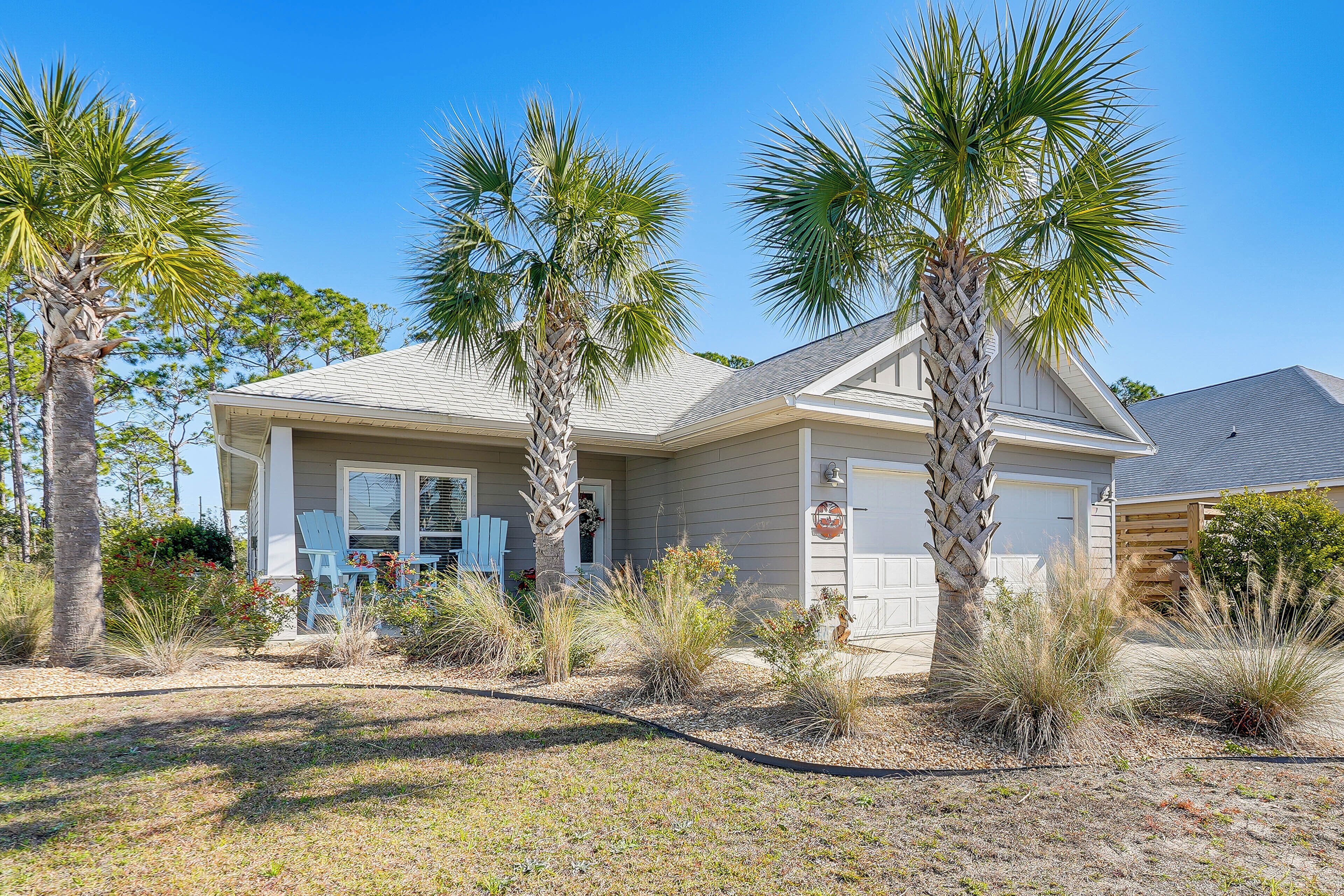 A single-story house with a garage, surrounded by palm trees and dry grass.