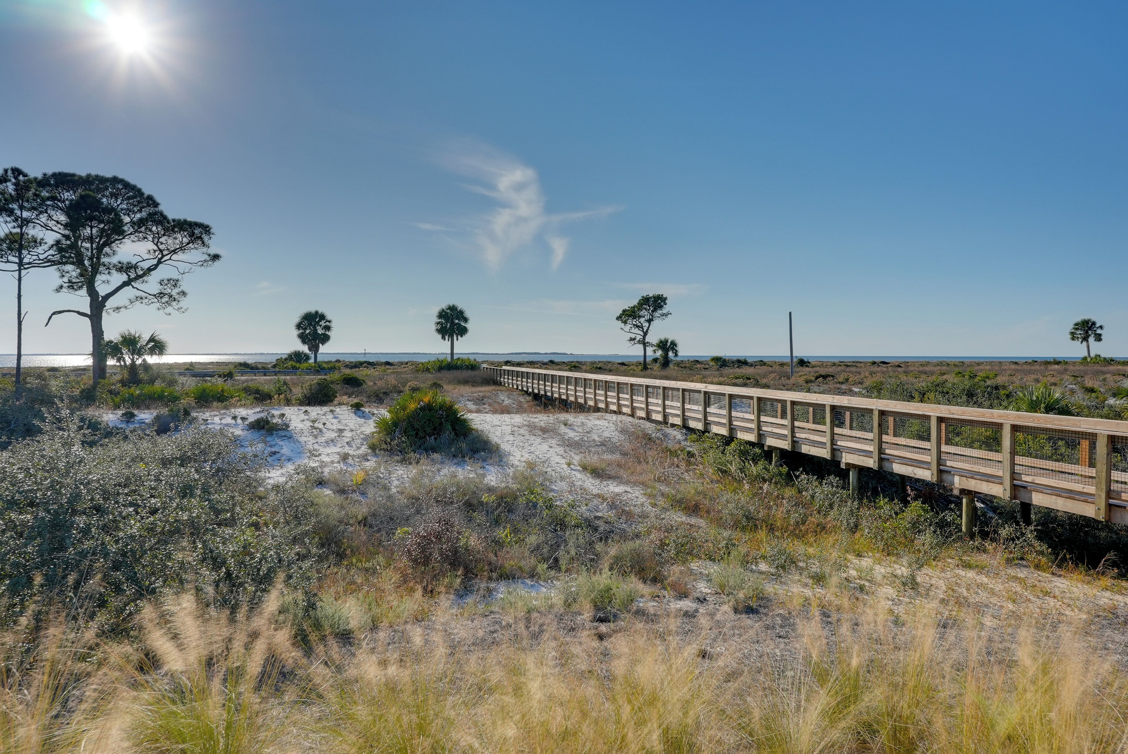 A wooden boardwalk along a beach with sparse vegetation and a clear sky.