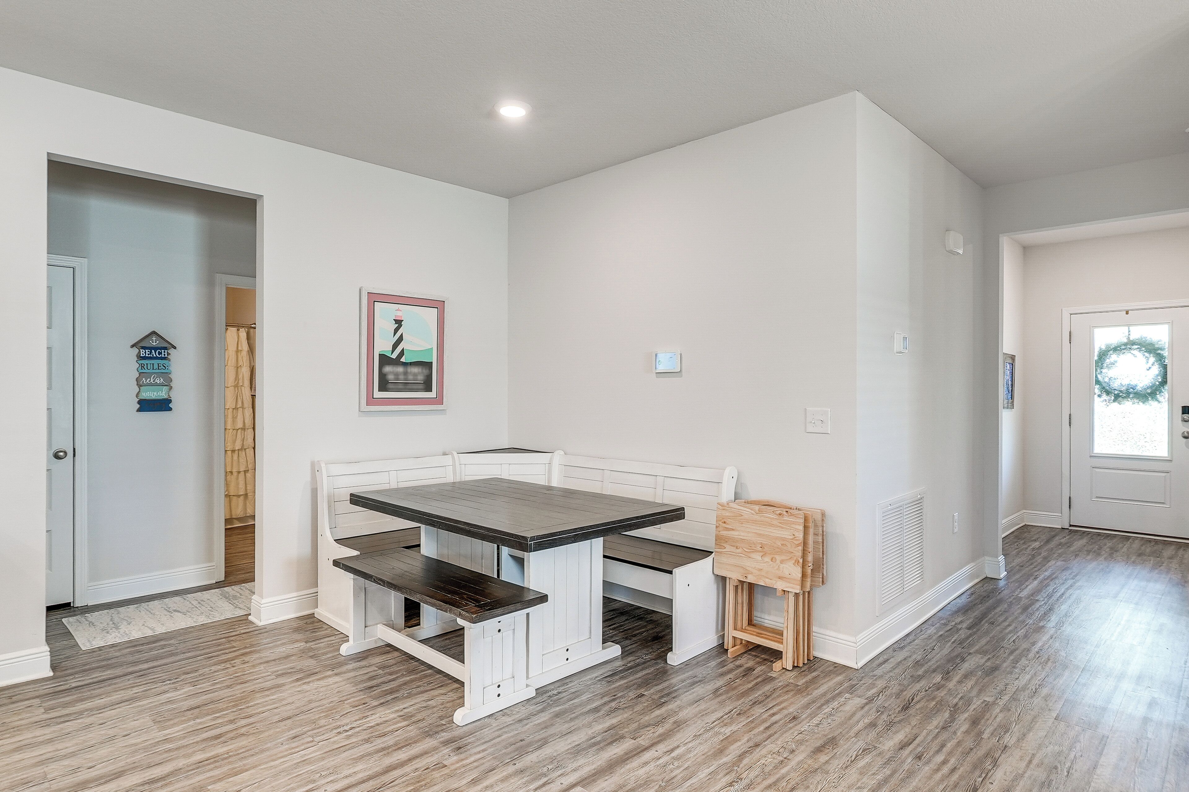 A dining area with a white bench and table, a small wooden stool, and a wall-mounted picture.