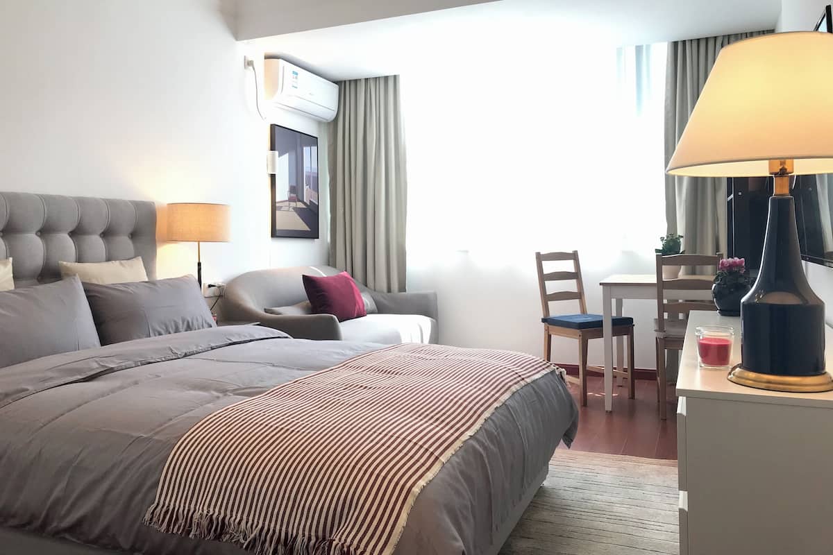 A hotel room with a large bed, a desk, a chair, a lamp, and a view of the outdoors.