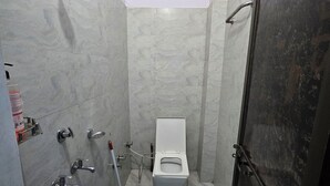 A small, tiled bathroom with a toilet, a shower, and a bucket. - Avadh Dham Guest House (Ayodhya)