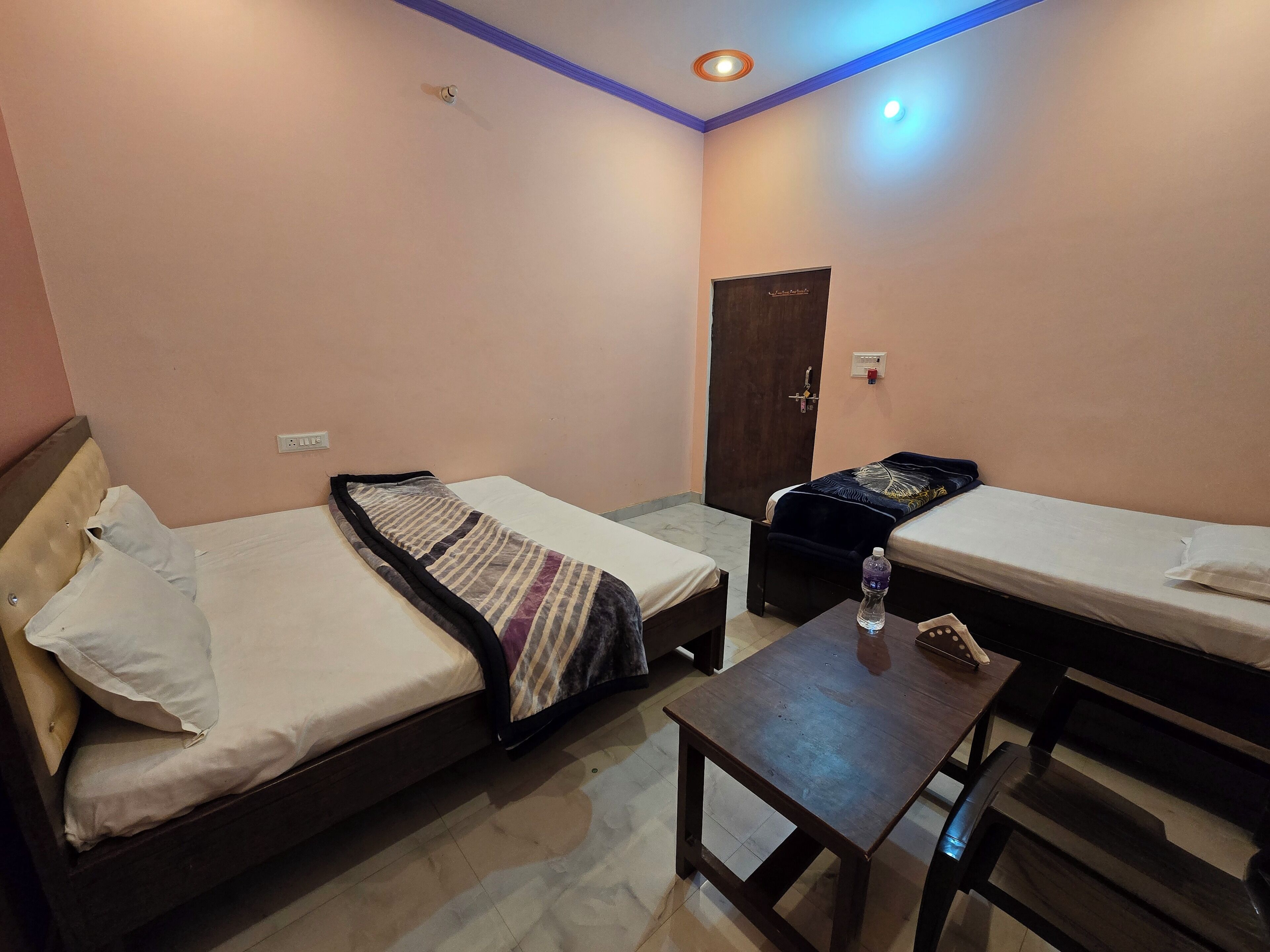 A small hotel room with two single beds, a wooden table, and a small desk.