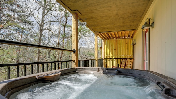 Een hottub met een houten terras en leuningen, omringd door bomen.