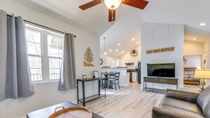 Een ruime woonkamer met een leren bank, een eethoek met tafel en stoelen, een keuken met televisie, en een plafondventilator.